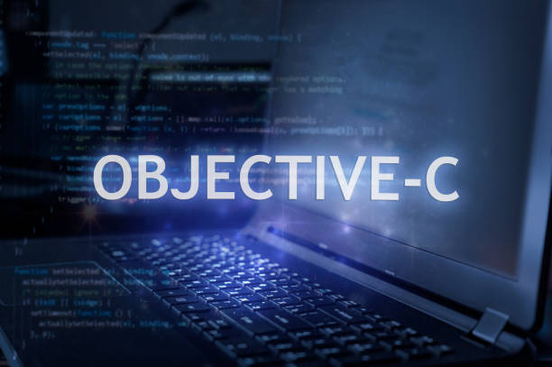 Objective-C inscription against laptop and code background. Learn programming language, computer courses, training.